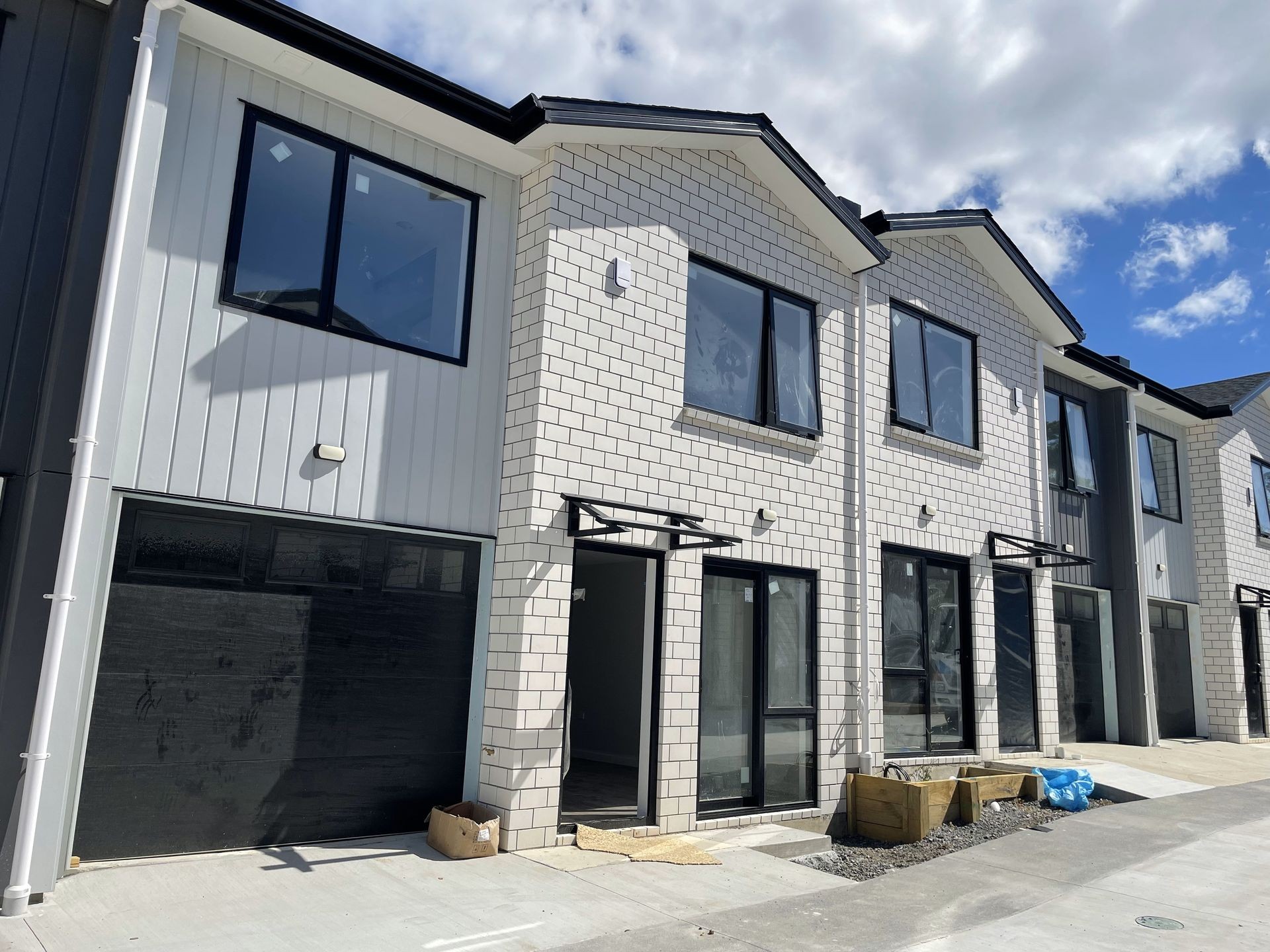 Newly constructed two-story townhouses with large windows and garage doors on a sunny day.