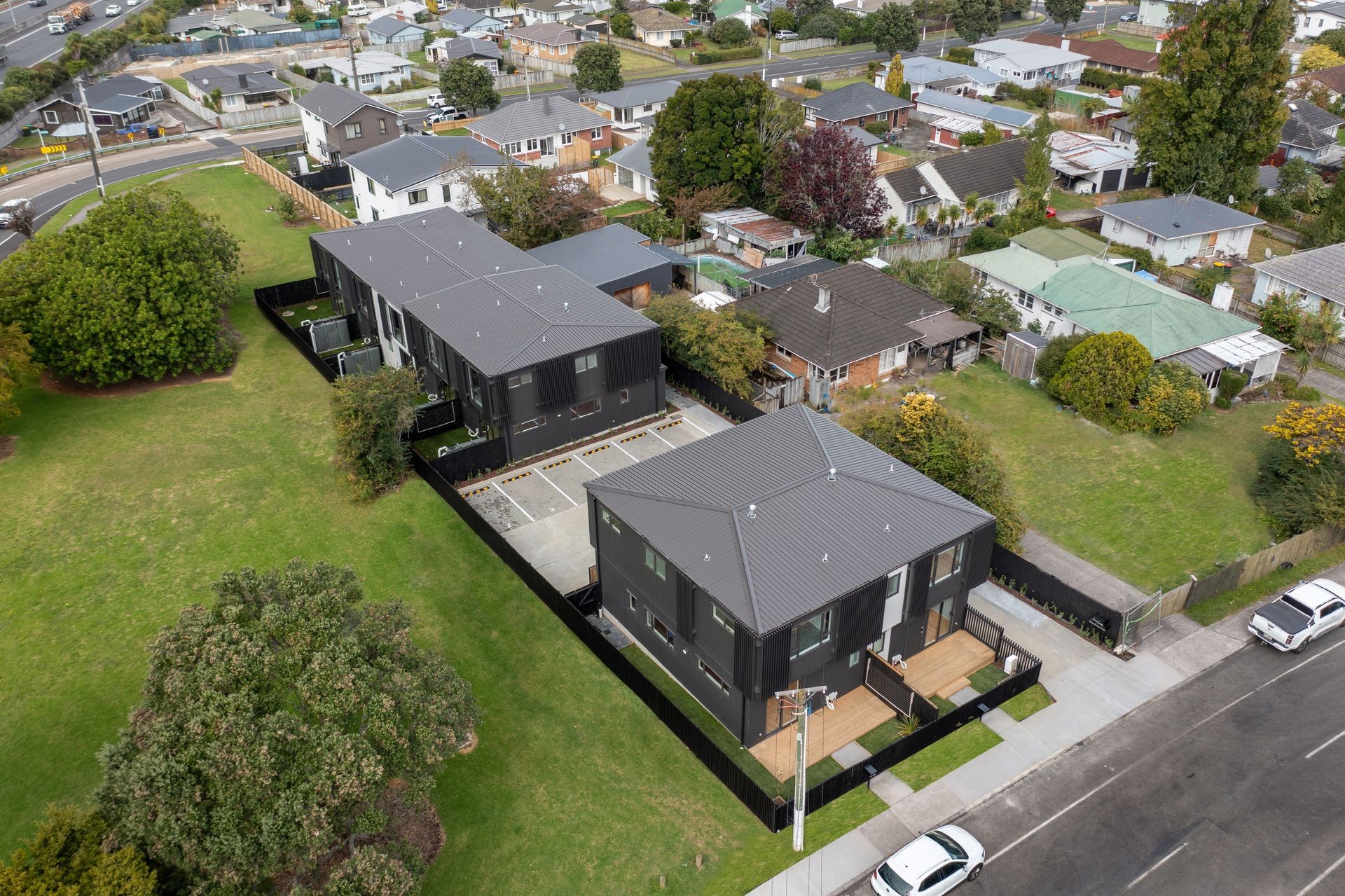Aerial view of a suburban neighborhood featuring new black-roofed apartment buildings surrounded by greenery.