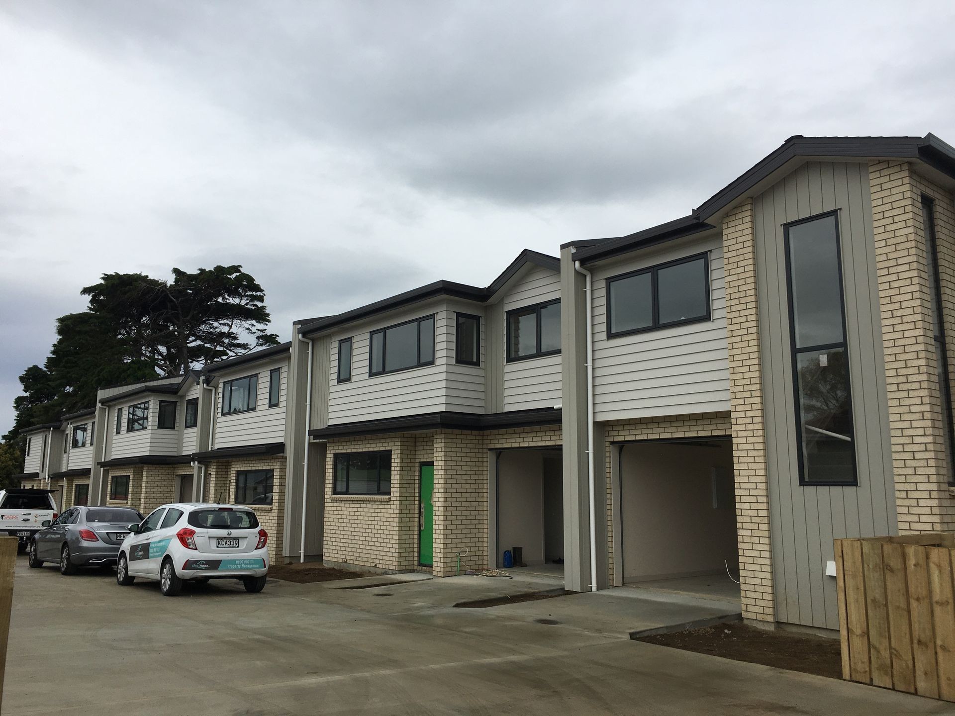Row of modern two-story townhouses with garages and parked cars on a cloudy day.