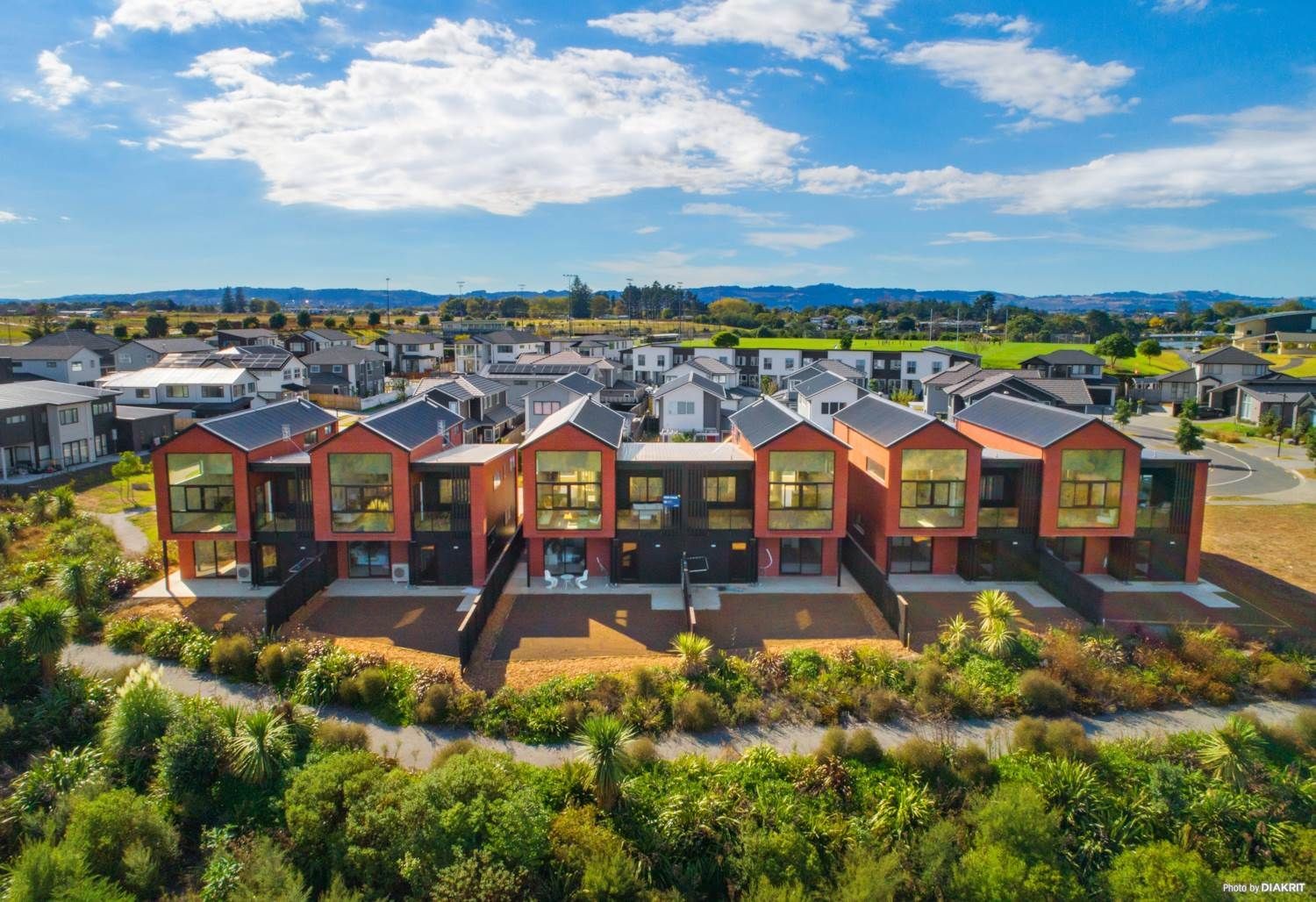 Aerial view of modern residential townhouses with large windows, surrounded by greenery and neighboring houses.