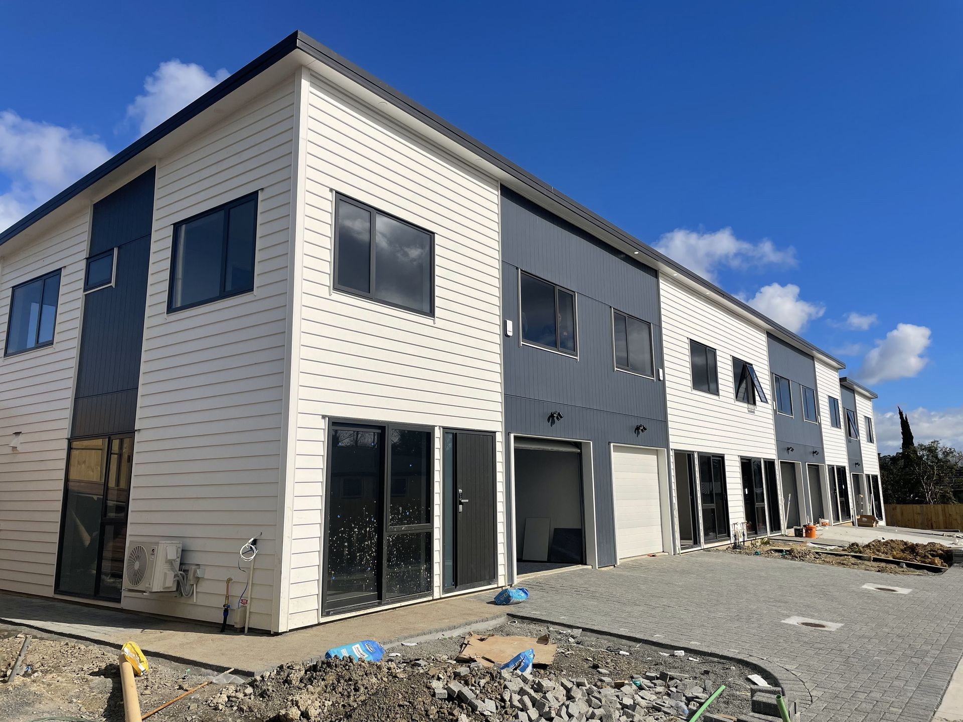 Row of newly constructed modern townhouses with white and gray exteriors under a blue sky.