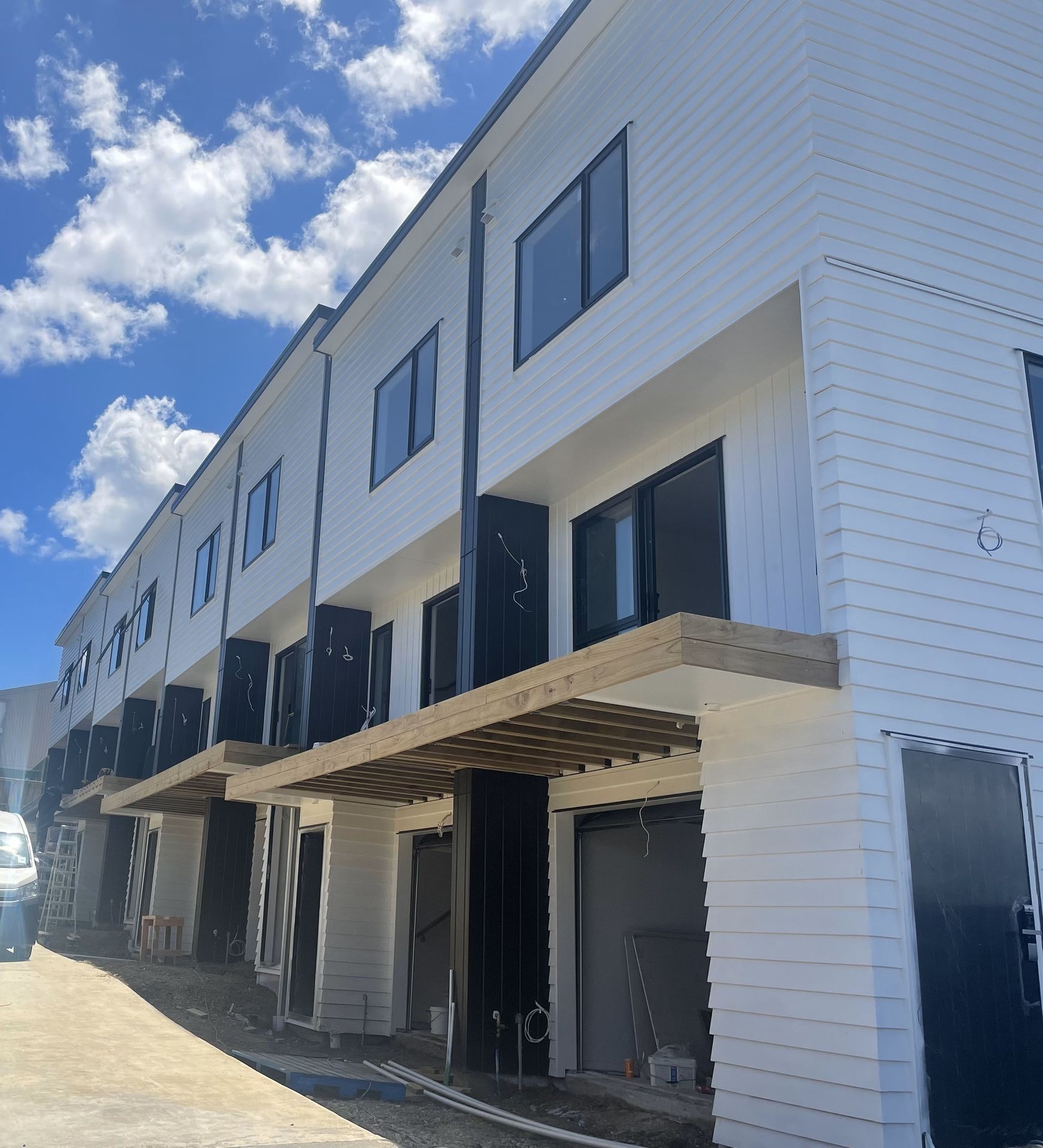 Row of modern, white townhouses under construction with blue skies and clouds in the background.