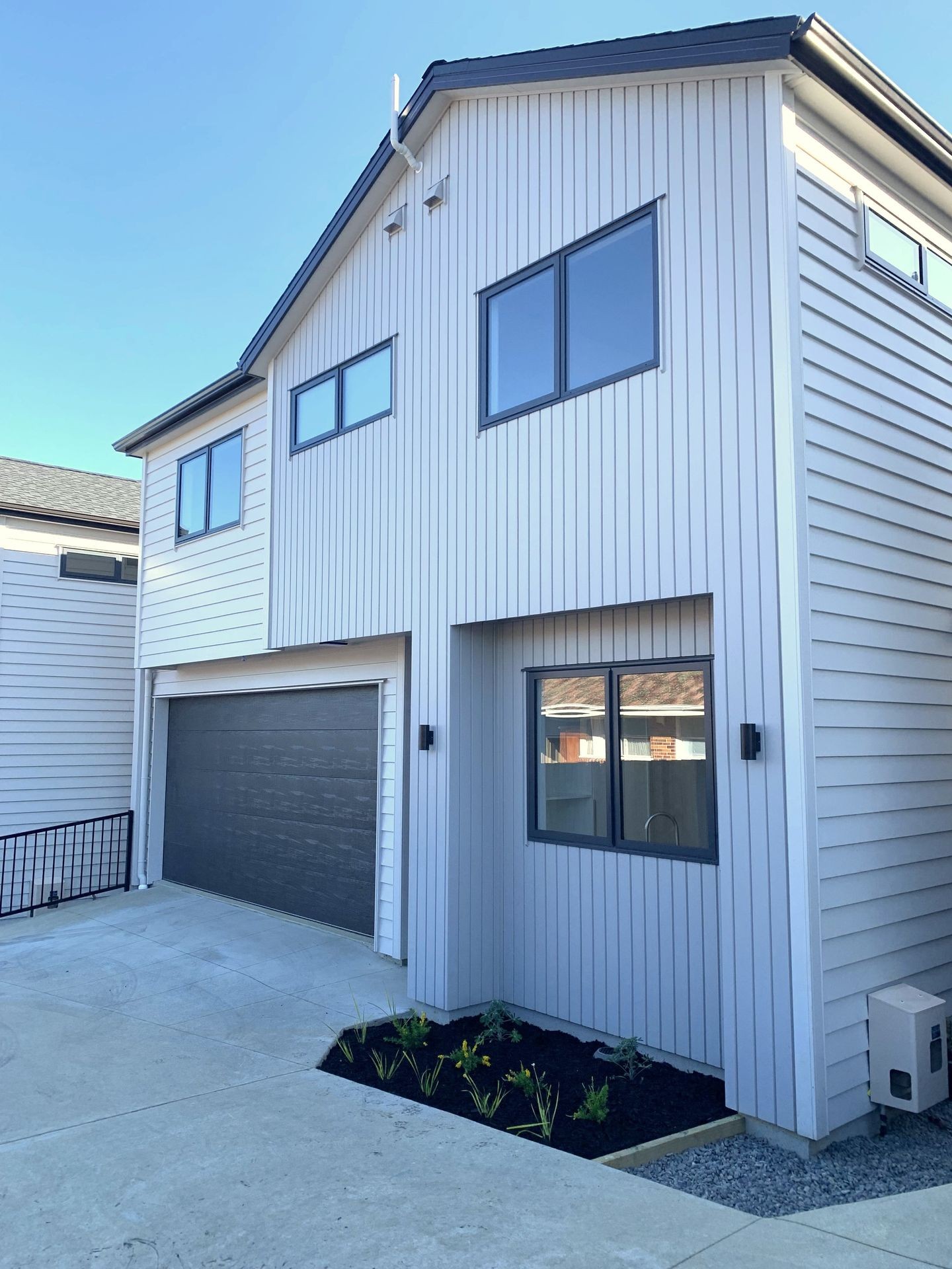 Modern two-story house with white vertical siding, large windows, and a gray garage door.
