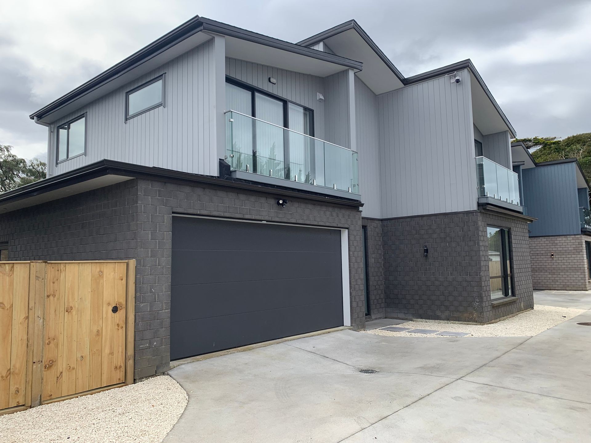 Modern two-story house with a gray exterior, large garage door, and glass balcony.